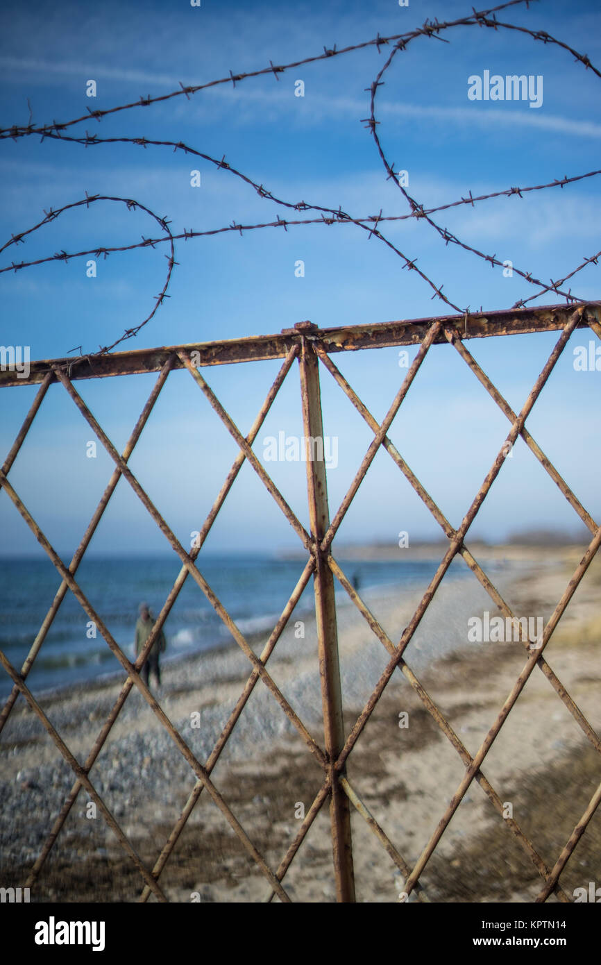 old barbed wire fence on the beach in front of blue water Stock Photo