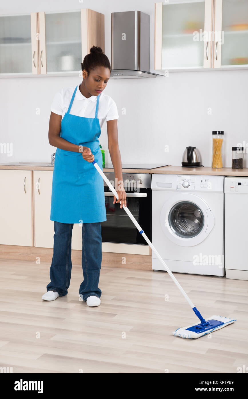 Young Female Janitor Mopping Hardwood Floor In Kitchen Stock Photo