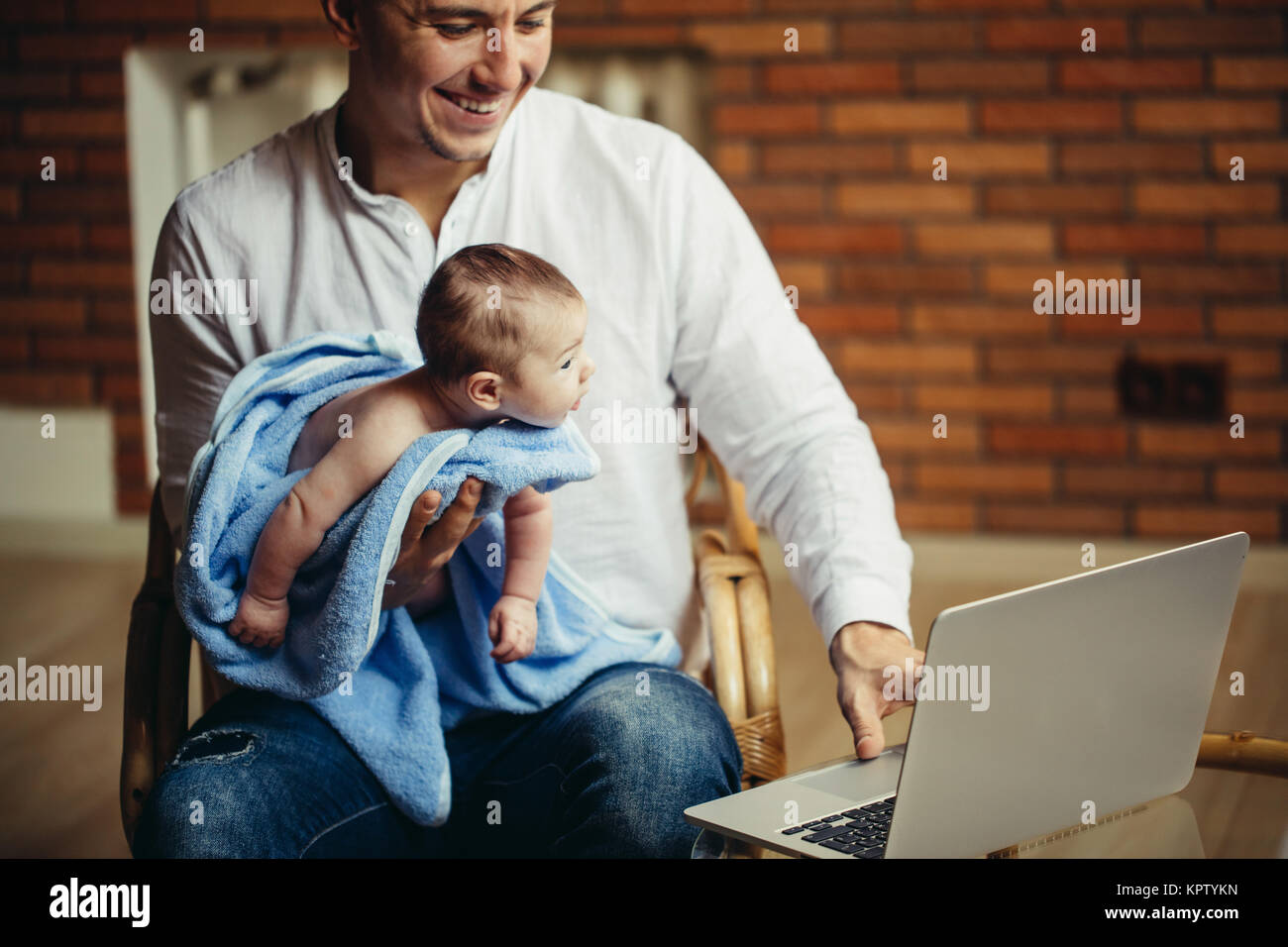 man working at desk at home with laptop, holding cute babys, looking at screen Stock Photo
