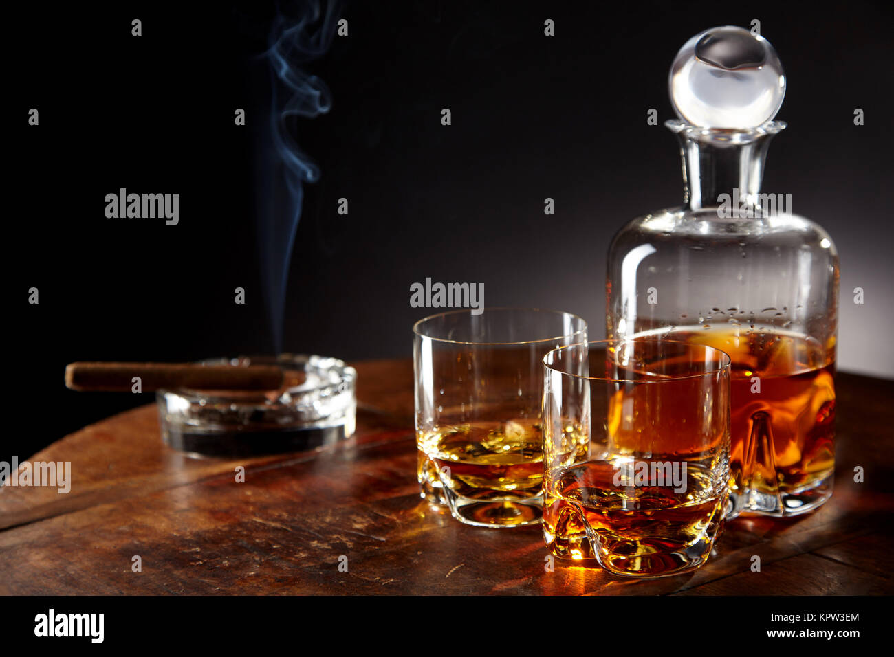 Decanter of alcohol by smoking cigar sitting in a round ashtray and two