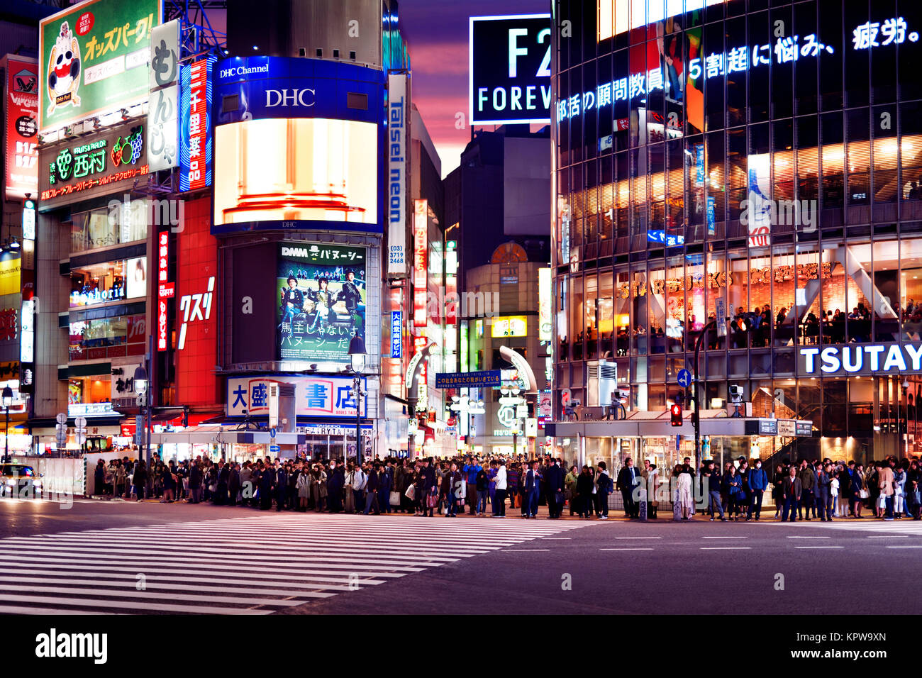 Crowd of people standing waiting for the green light to start crossing the World's biggest and busiest interesection at Shibuya station lit with stree Stock Photo