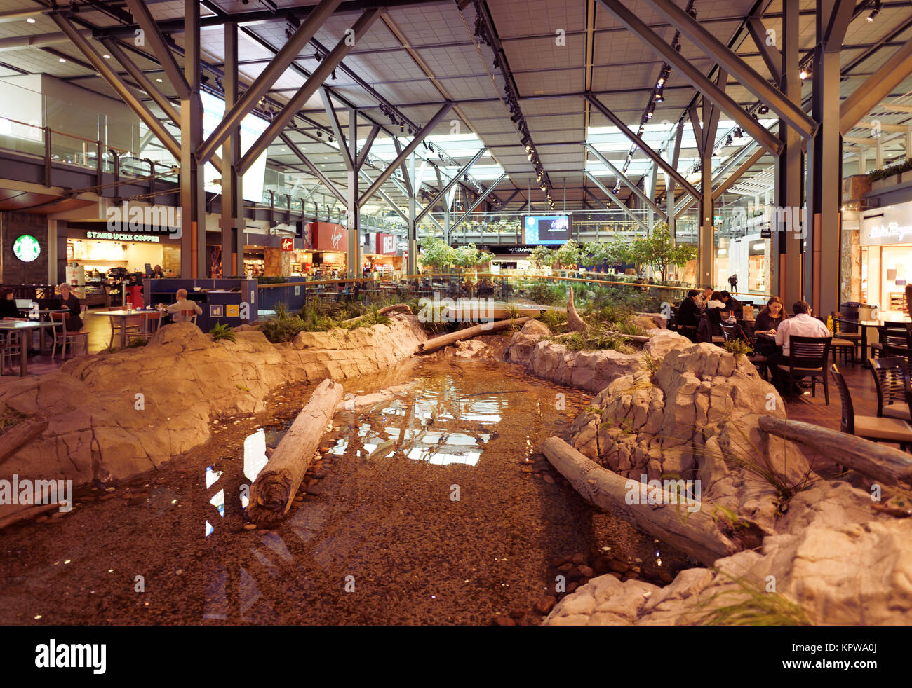 People in a waiting lounge of Vancouver International Airport, departures interior with restaurants and a beautiful resting area with an artificial po Stock Photo