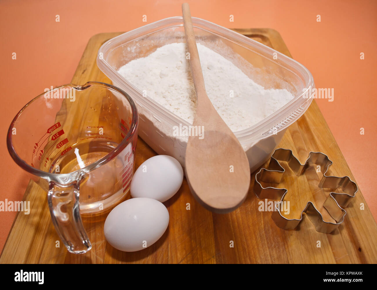 Baking utensils, a cookie cutter, a container of flour, two eggs and a