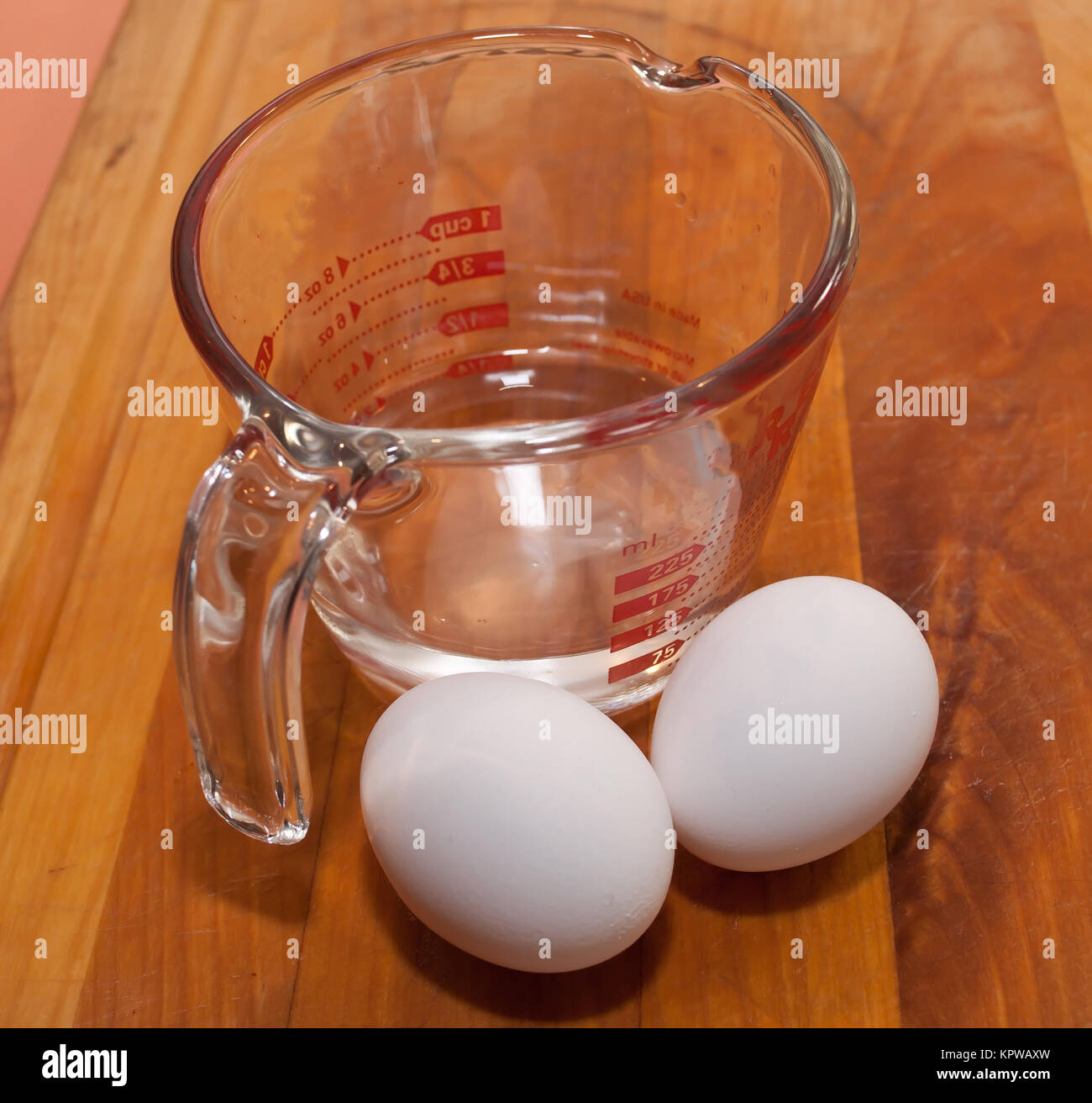 https://c8.alamy.com/comp/KPWAXW/two-eggs-next-to-a-glass-measuring-cup-on-a-wooden-cutting-board-KPWAXW.jpg
