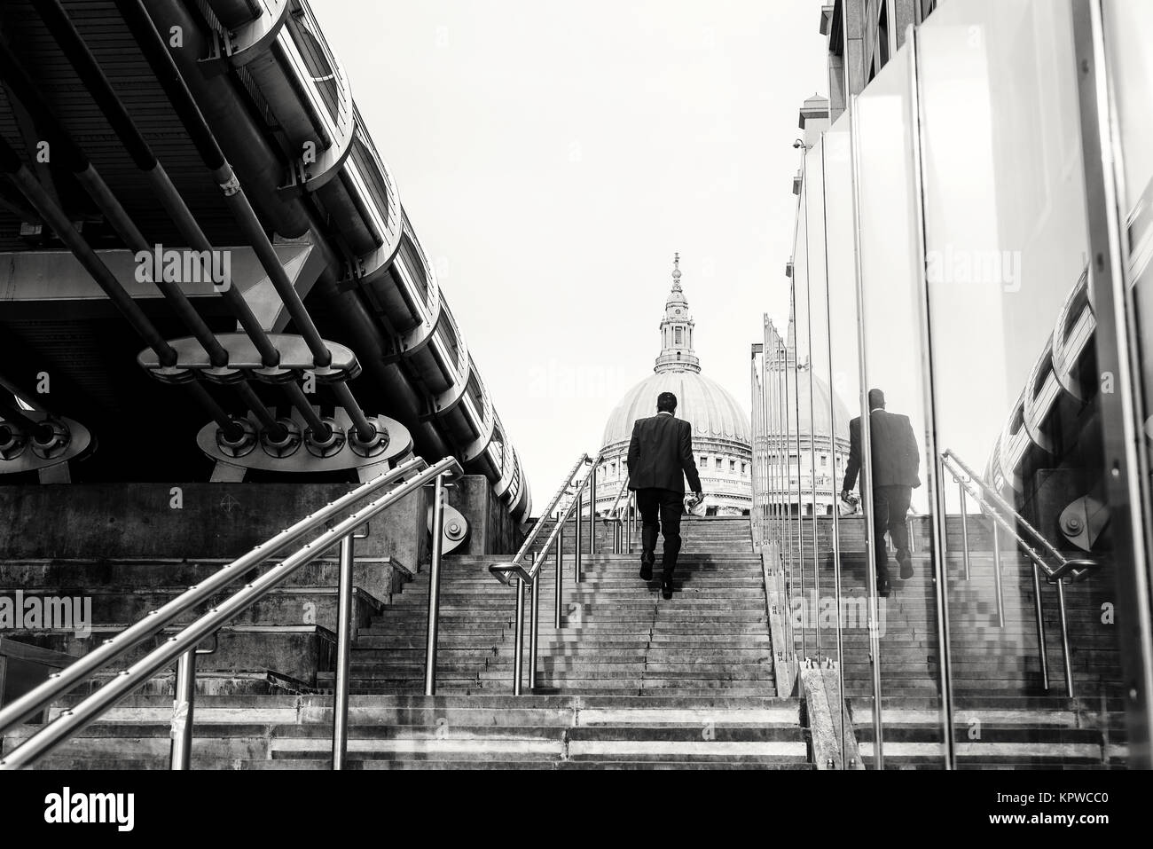 Man in business suit walking up steps towards St Paul’s Cathedral in London England in black and white Stock Photo