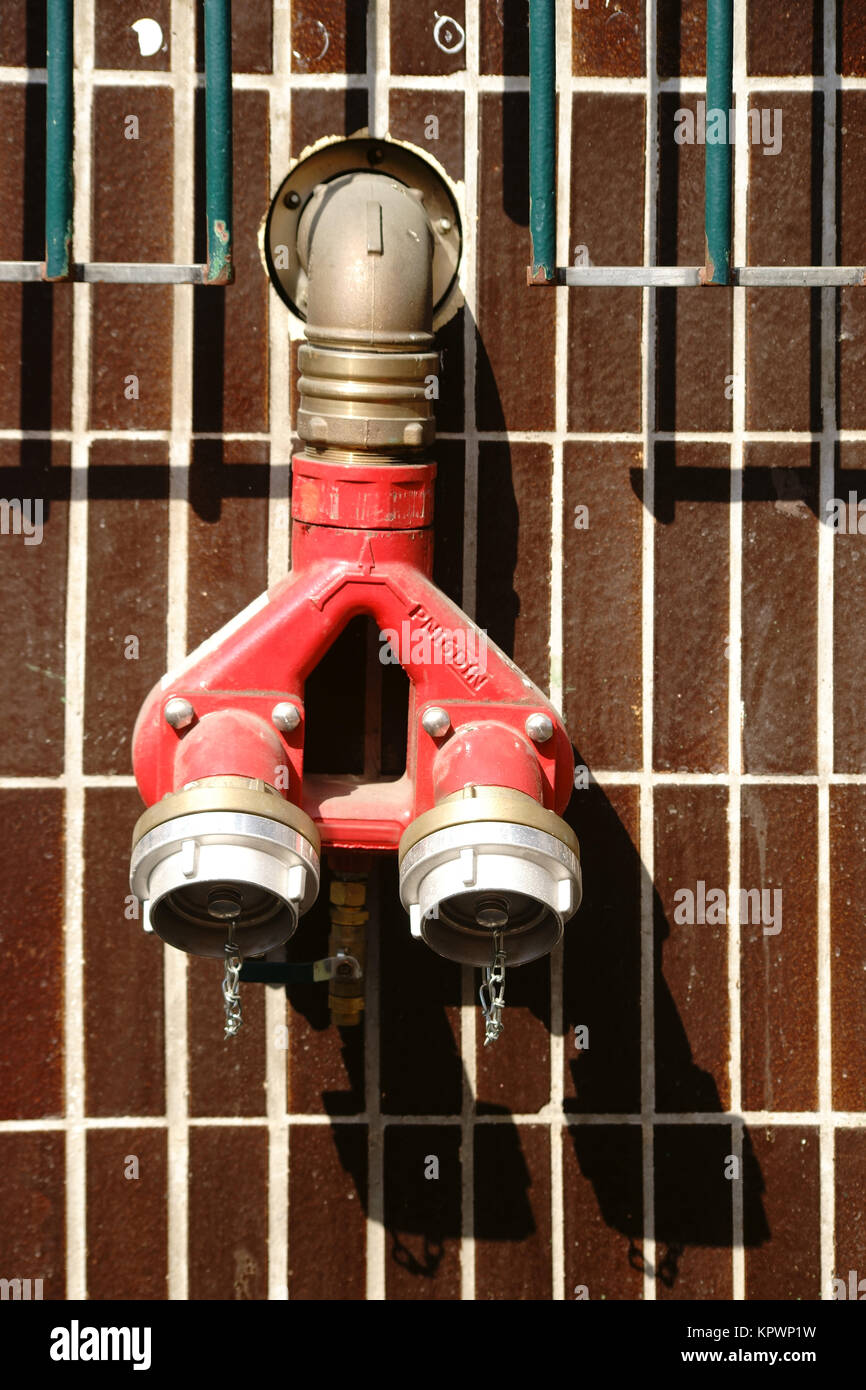 Die Nahaufnahme eines Feuerhydranten mit Wasseranschlüssen an einer gefliesten Wand. Stock Photo