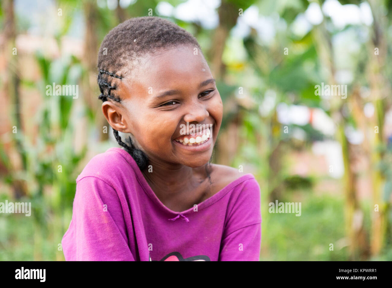 A beautiful laughing Ugandan girl sitting on a fallen tree trunk. Stock Photo