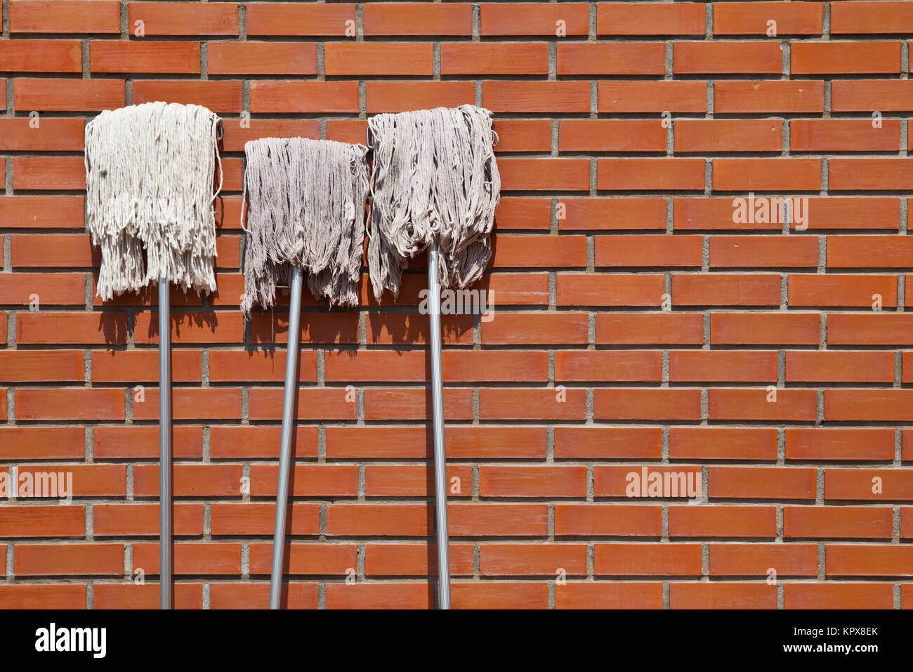 three white mops lean against red brick wall revealed to sunlight