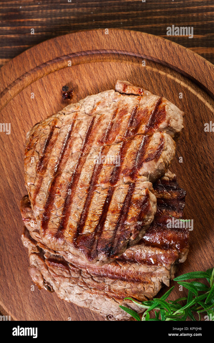 Succulent portions of grilled fillet mignon served with rosemary on an wooden board. Top view Stock Photo
