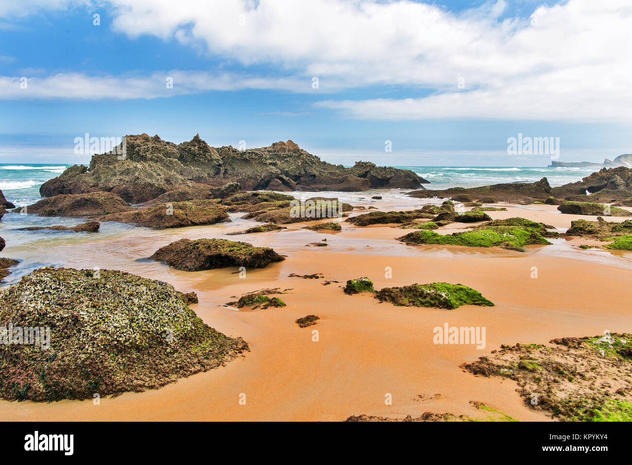 Strip of big stones on the sandy beach during an outflow. Black and gray stones, yellow sand and water of the ocean in the distance. Sunny summer day Stock Photo