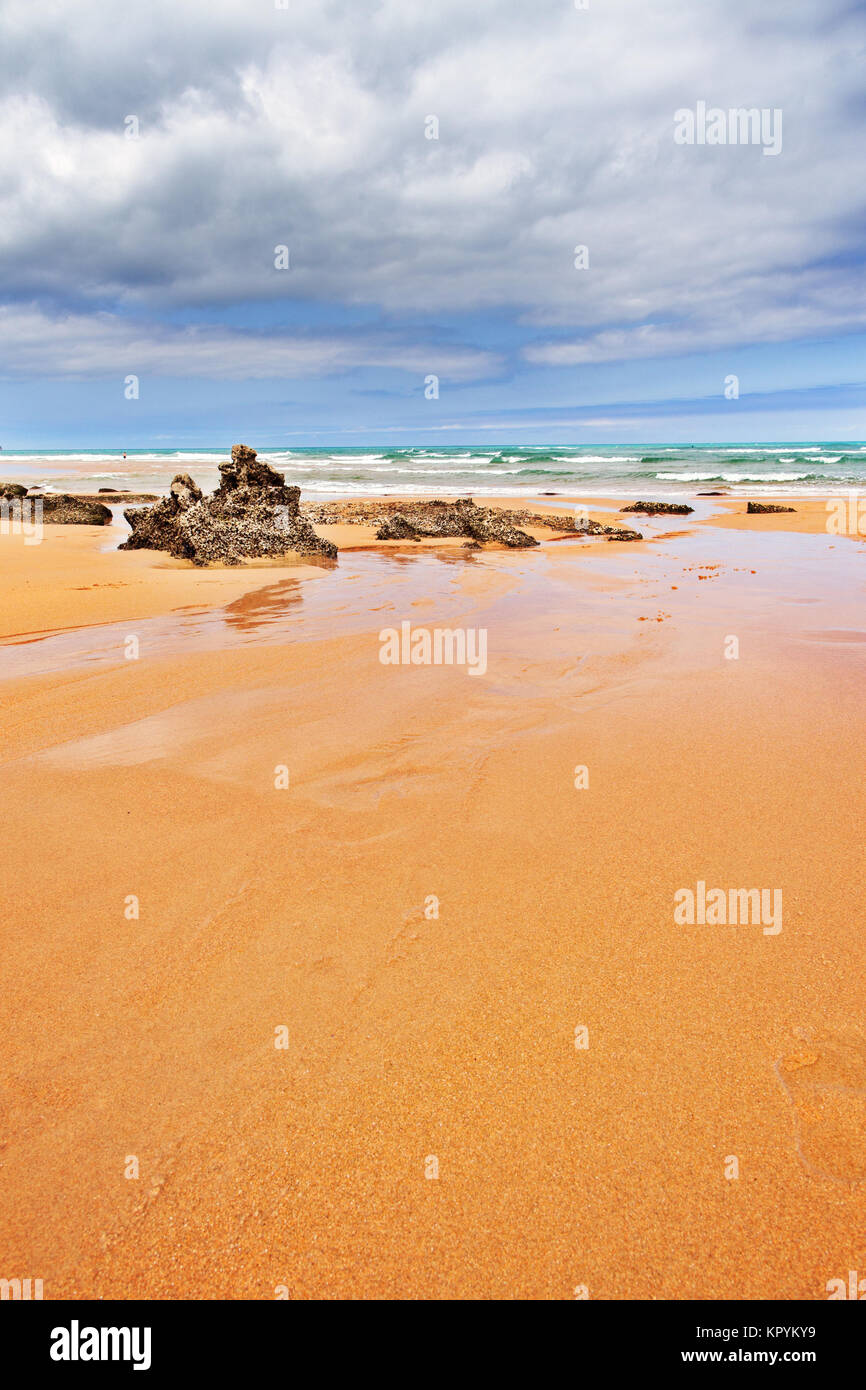 Strip of big stones on the sandy beach during an outflow. Black and gray stones, yellow sand and water of the ocean in the distance. Sunny summer day Stock Photo