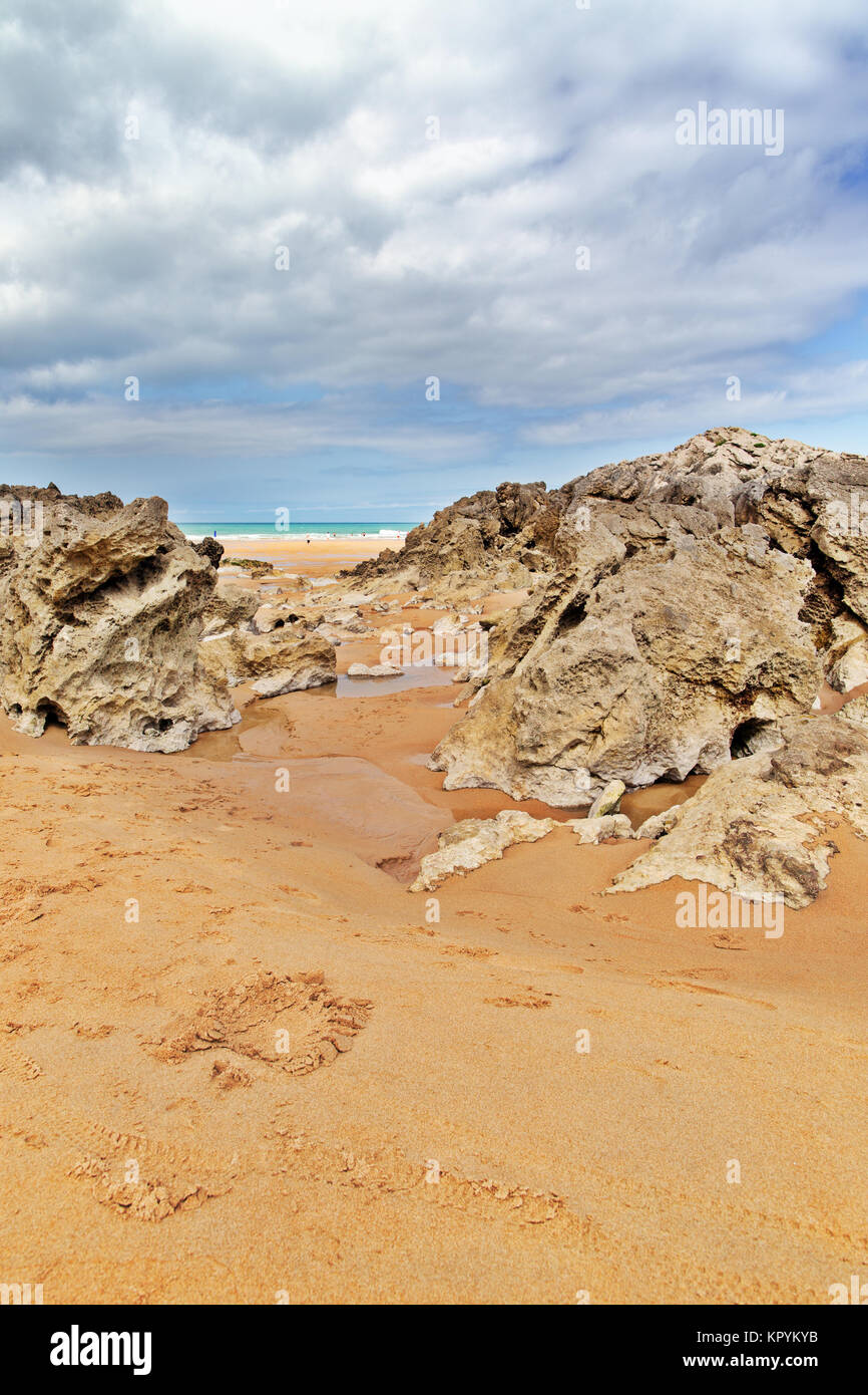 Strip of big stones on the sandy beach during an outflow. Black and gray stones, yellow sand and water of the ocean in the distance. Sunny summer day Stock Photo