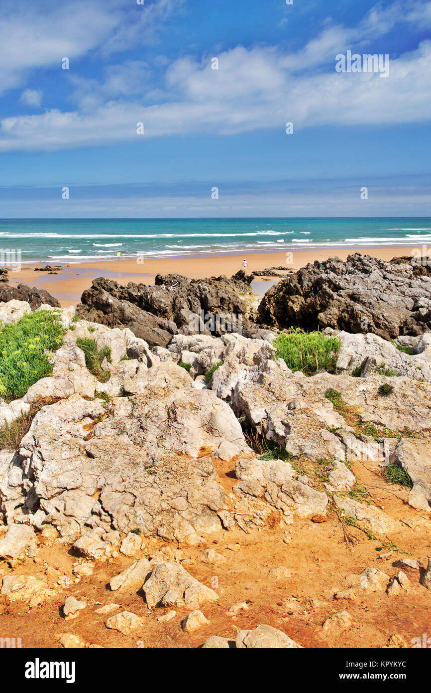 Strip of big stones on the sandy beach during an outflow. Black and gray stones, yellow sand and water of the ocean in the distance. Sunny summer day Stock Photo
