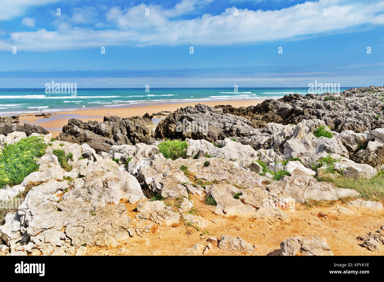 Strip of big stones on the sandy beach during an outflow. Black and gray stones, yellow sand and water of the ocean in the distance. Sunny summer day Stock Photo