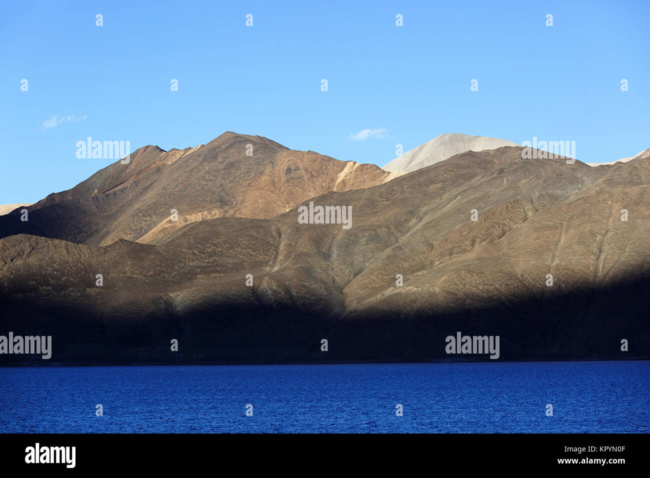 Shadow of peaks at barren landscape and the himalayan mountains by the blue lake of Pangong Tso, Ladakh, Jammu and Kashmir, India. Stock Photo