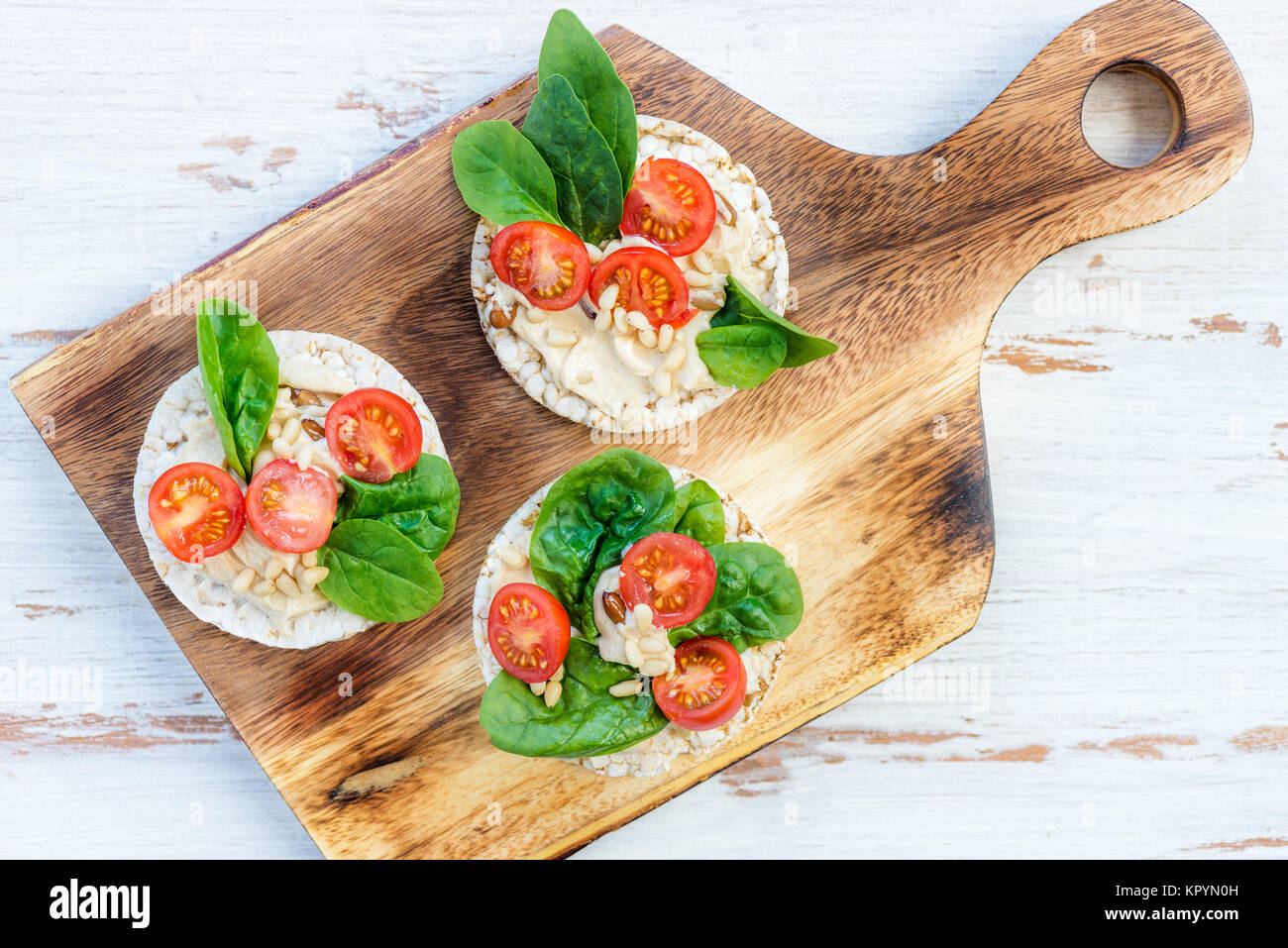 Healthy Snack from Rice Cakes with Hummus, Spinach and Tomatoes on