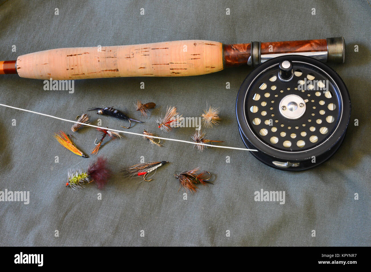 Custom bamboo fly rod, reel, line and an assortment of flies for trout fishing on a green canvas background. Stock Photo