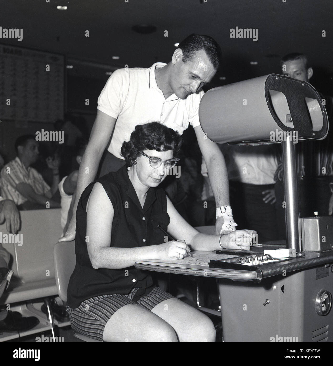 1960s, historical, man looks over a lady's shoulder as she marks down the scores sitting at a booth at a ten-pin bowling alley, USA. Stock Photo