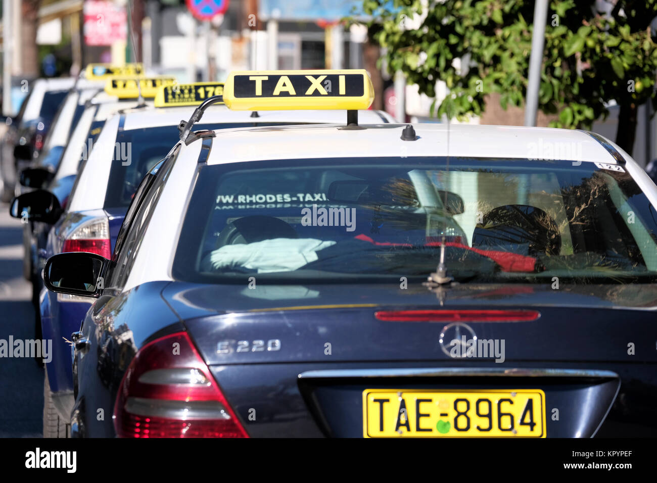 A row of similar liveried  taxi's or cabs waiting on a taxi rank for hire. All are displaying taxi signs and are waiting to be hailed or hired Stock Photo
