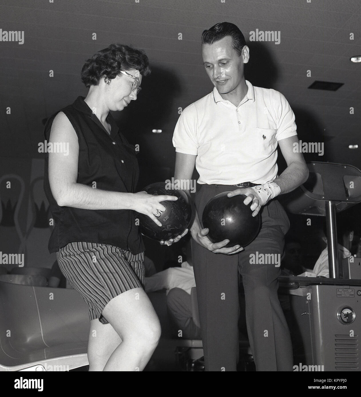 1960s, historical, man showing a lady the correct way fingers should be placed into the slots in a bowling ball at a ten-pin bowling alley, USA. Stock Photo