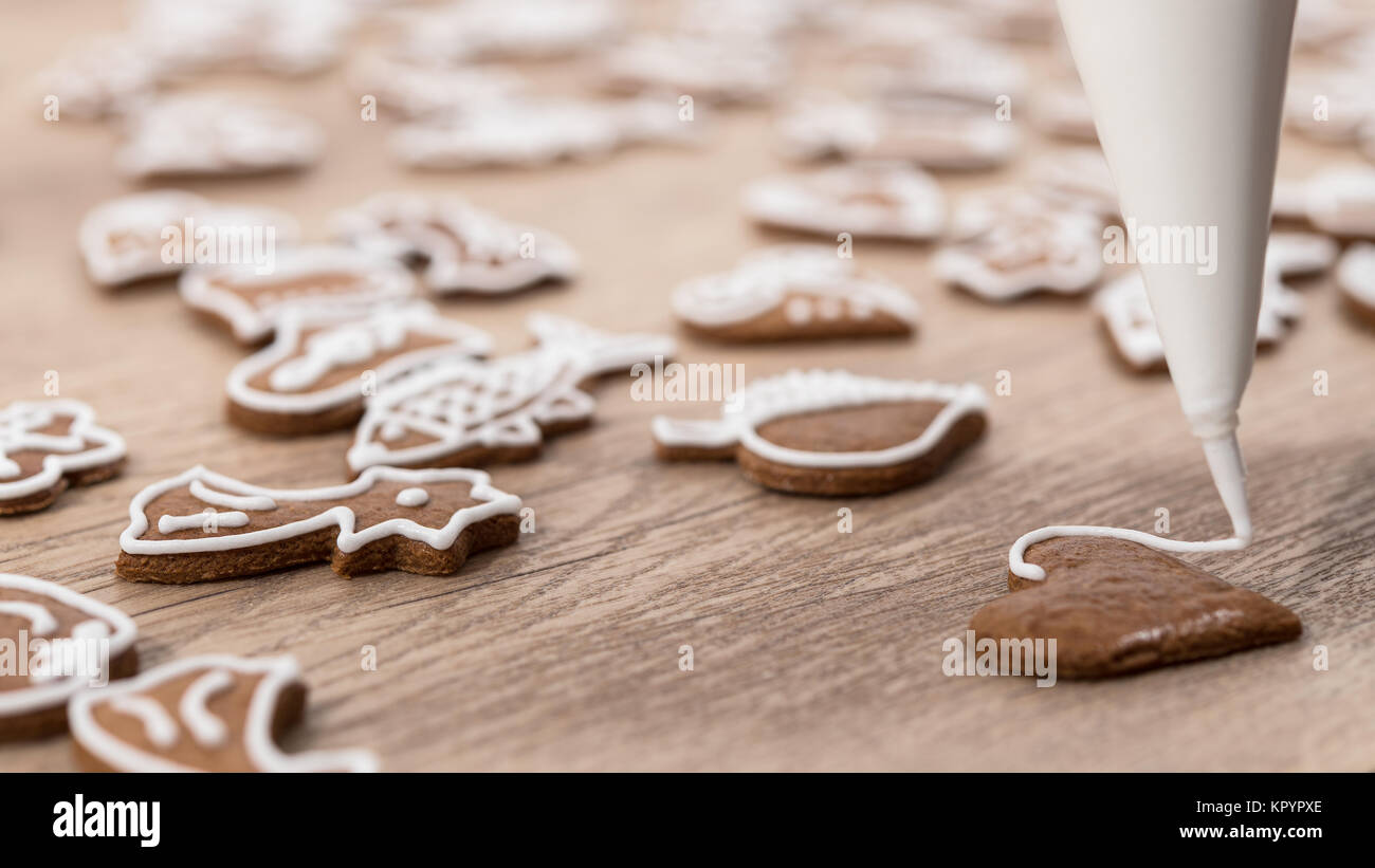 Close-up of decorating christmas gingerbread in heart shape. Painting of pastry using icing bag with sugar frosting on wood. Small depth of sharpness. Stock Photo