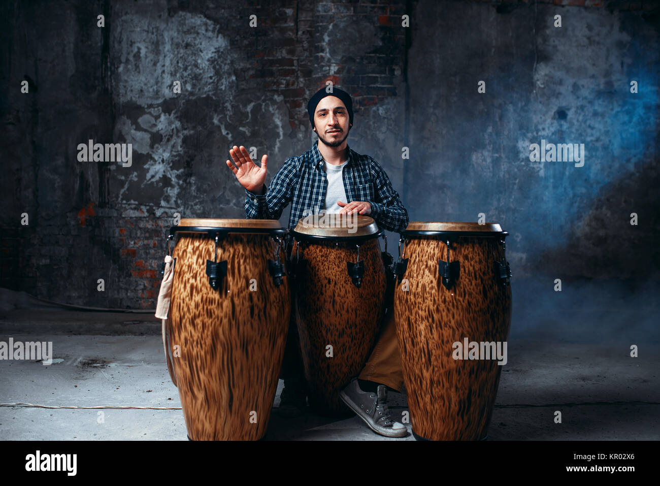 Male drummer playing on wooden bongo drums in factory shop, musician in motion. Djembe, musical