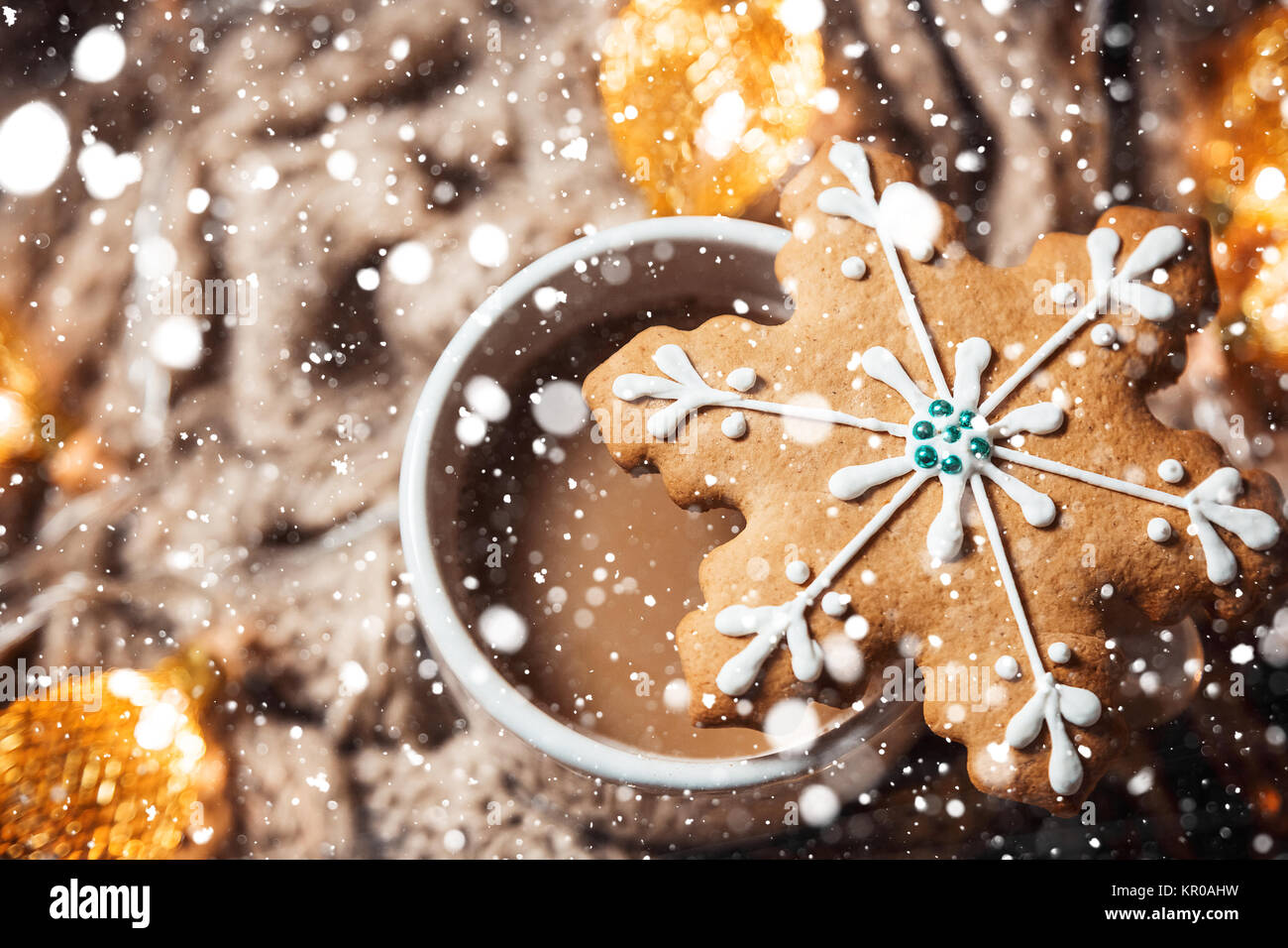 Christmas background with coffee in a white cup and gingerbread snowflakes on a brown knitted winter scarf and a glowing golden garland. Beautiful con Stock Photo