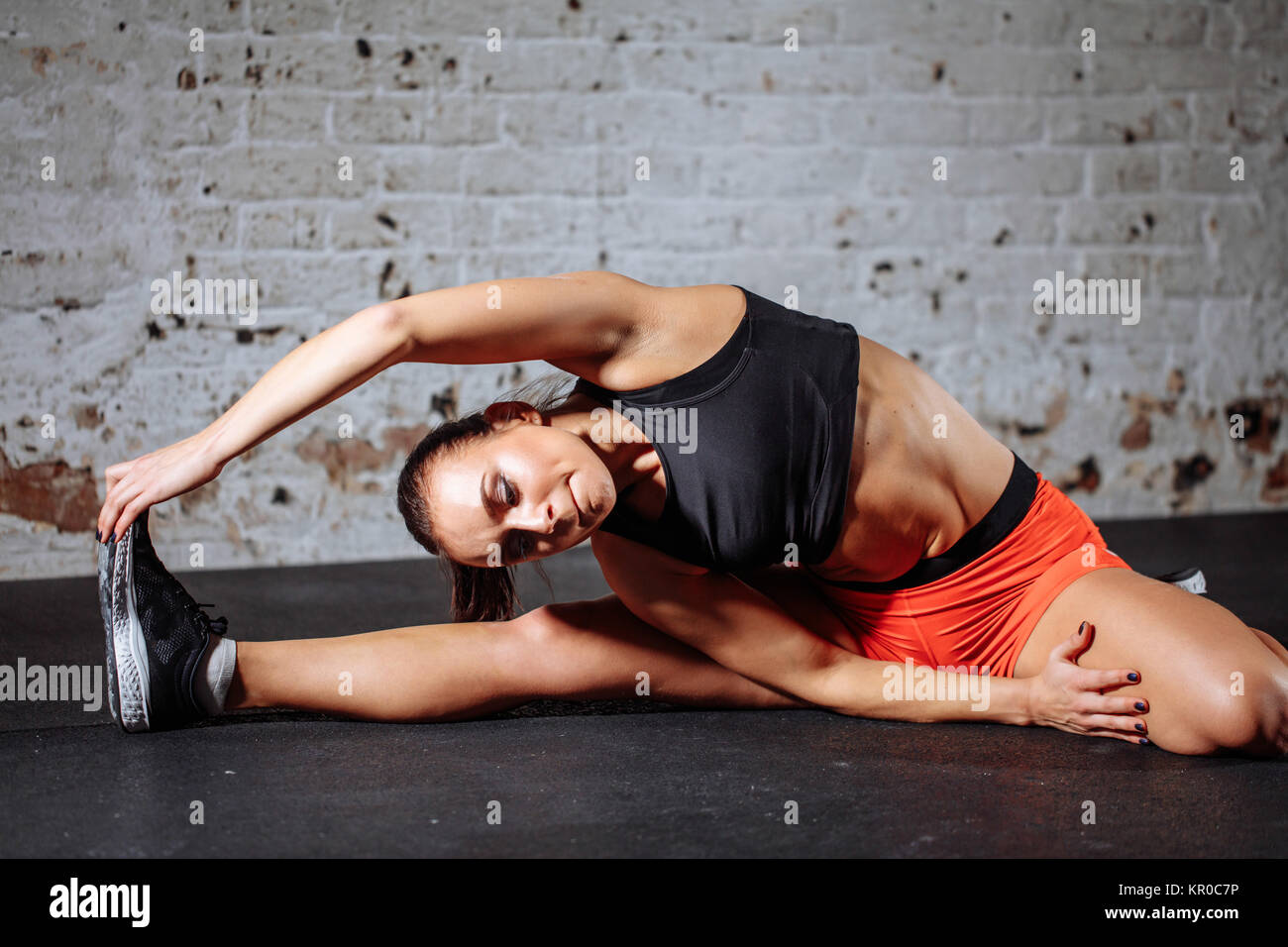Wnba Stretchig woman sport stretching in gym with brick wall and black mats Stock ...
