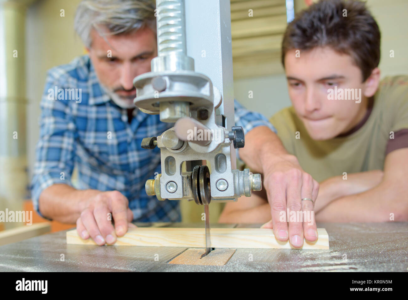 Apprentice carpenter watching how to use bench saw Stock Photo Alamy