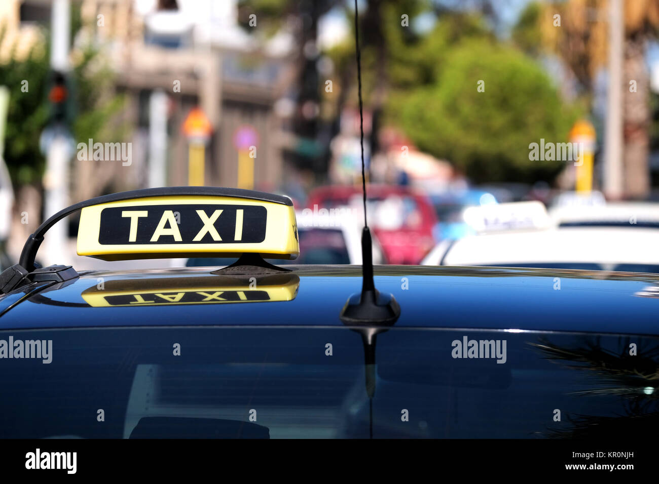 A close up of a taxi for hire sign on top of a cab. It's waiting on a taxi rank on a busy street to be hired or hailed by a customer Stock Photo