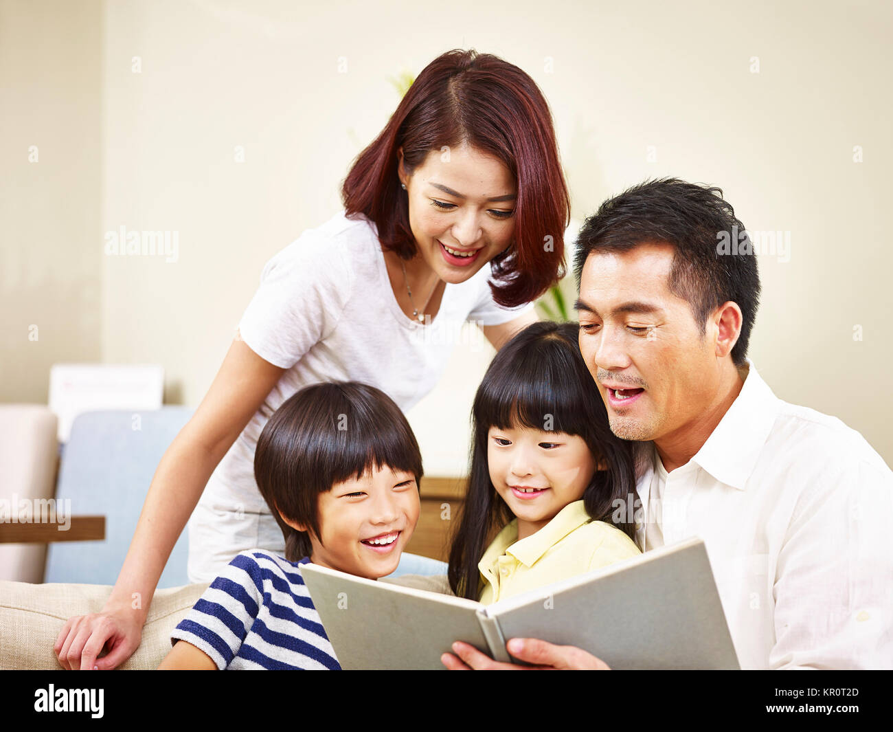 happy asian family with two children sitting on sofa reading a book together. Stock Photo