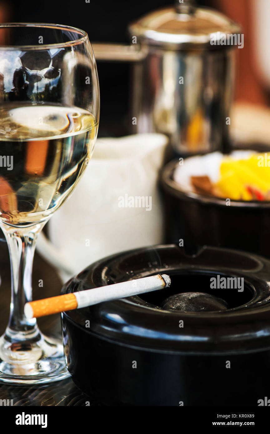 a glass and a cigarette Glass of White Wine With an Ashtray and Cigarette on a Table In a Cafe or  Restaurant Stock Photo