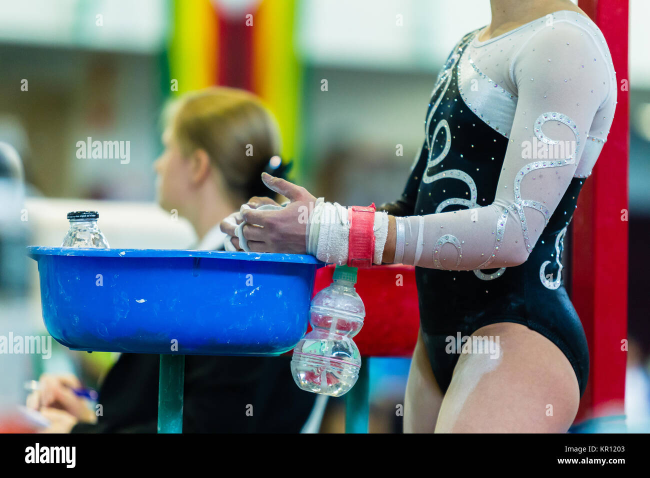 Gymnastics girl gymnast chalking hands leather wrist straps at chalk basin for parallel bars