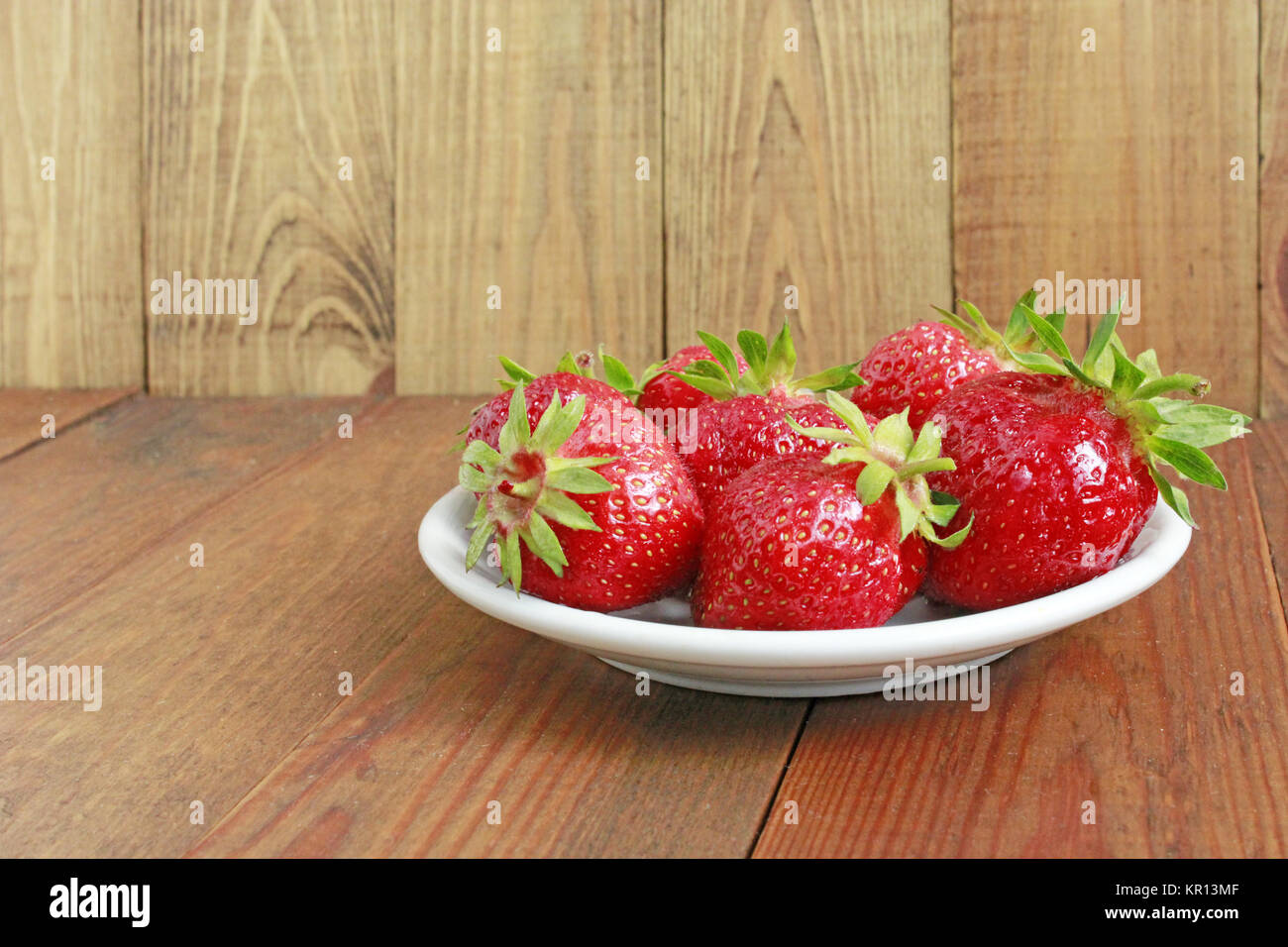 ripe red strawberries on the white plate on the brown Stock Photo - Alamy