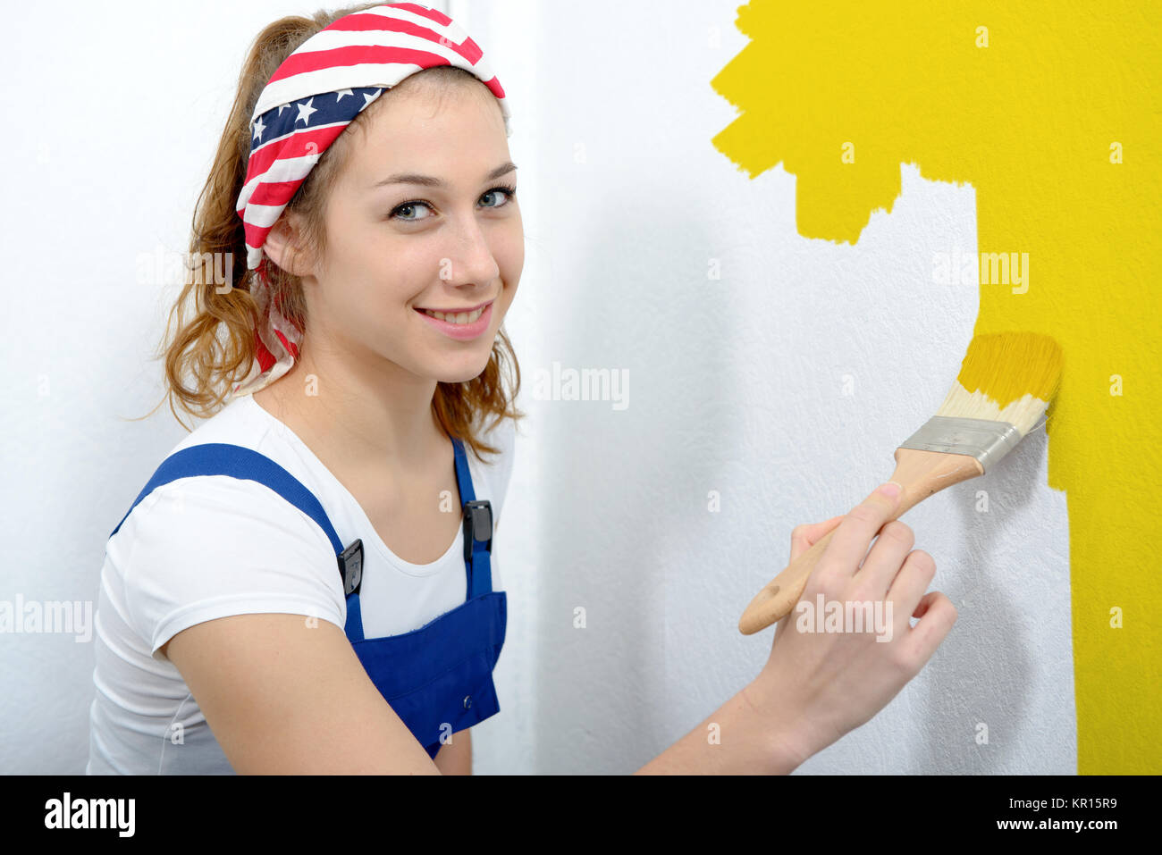 a pretty young woman painting the wall yellow color Stock Photo - Alamy