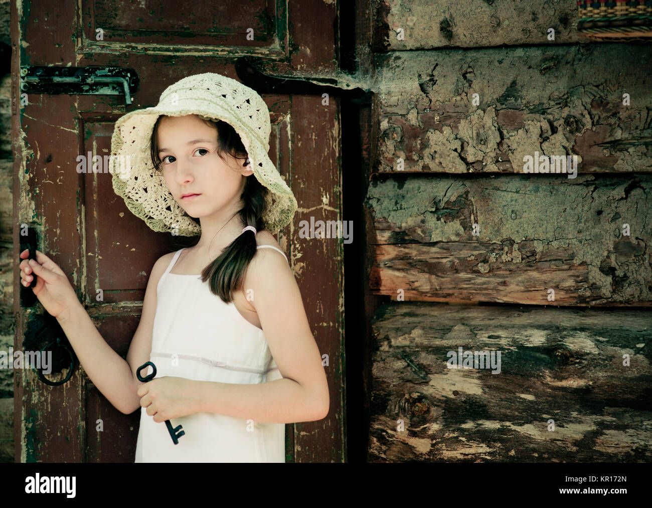 Pretty young girl standing at the door outside an old wooden hut and ...