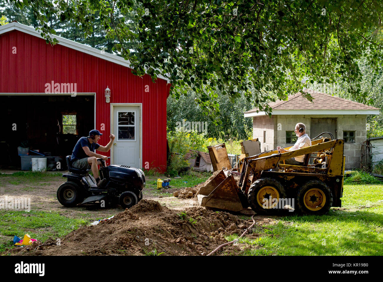 Adult father and son head to head with skid steer and lawn mower Stock Photo