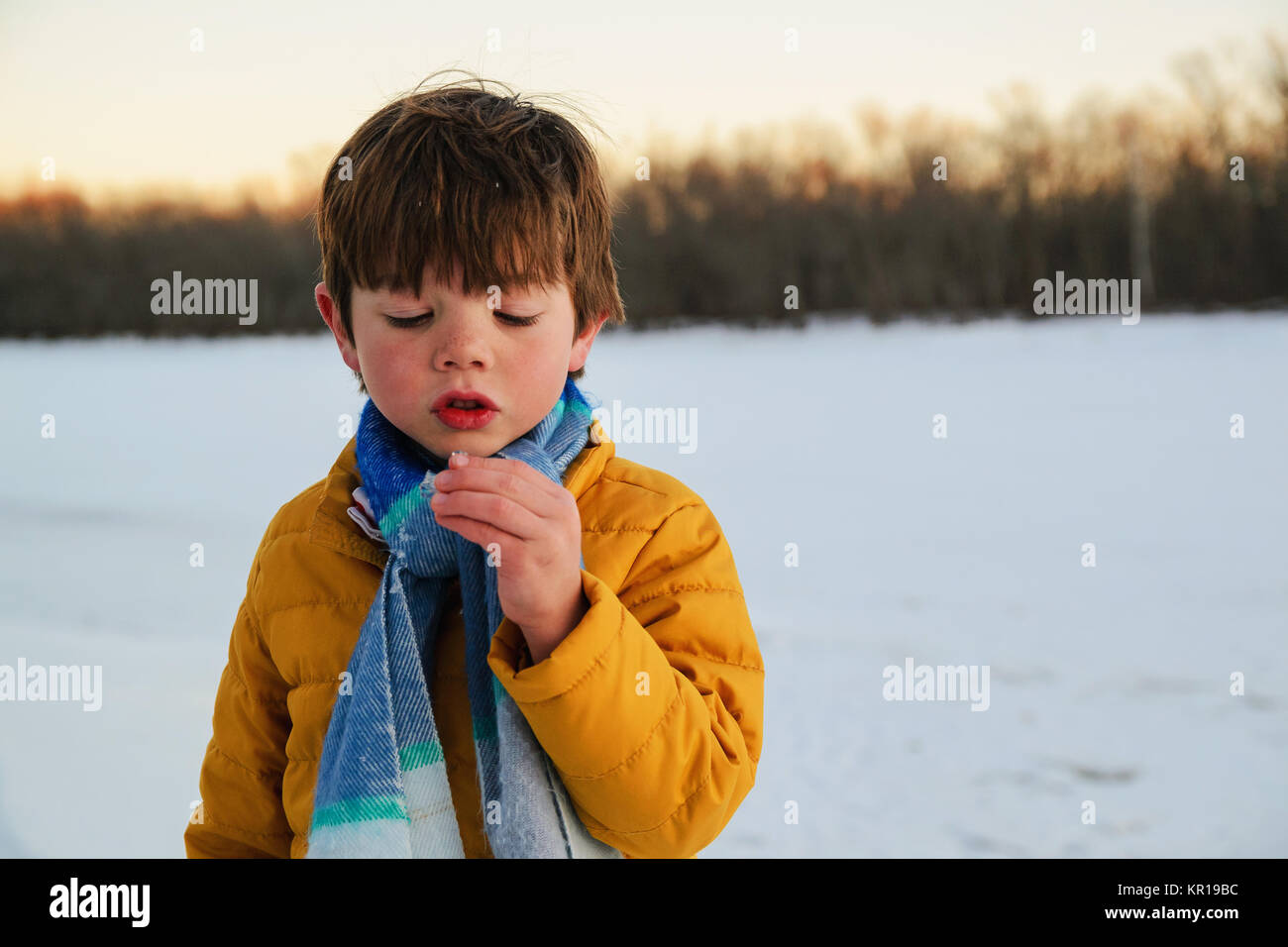 Boy standing on a frozen lake looking at piece of ice Stock Photo