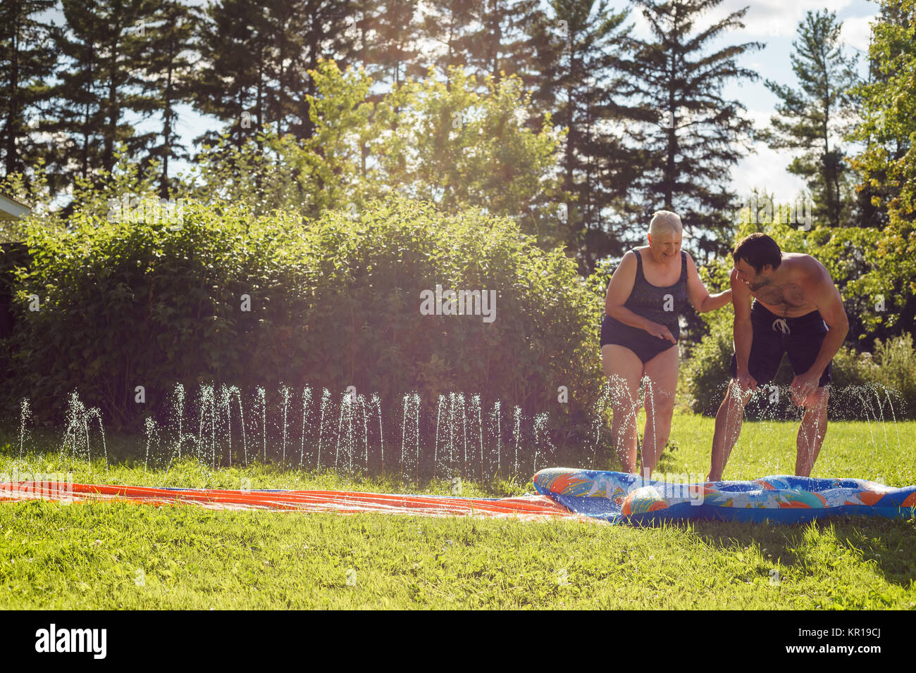 Man and his mother playing on a slip and slide in the garden Stock Photo