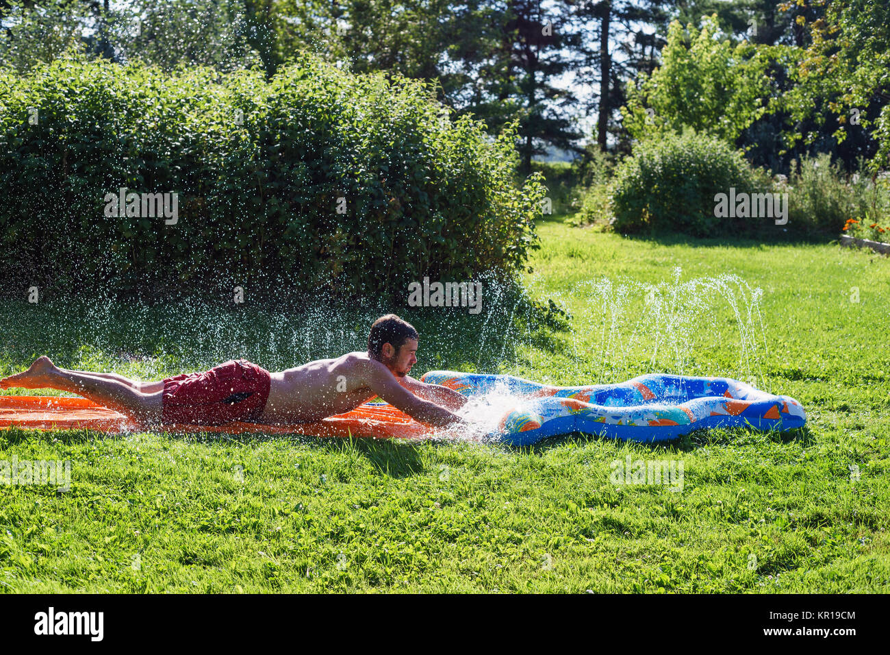 Man playing on a slip and slide in the garden Stock Photo