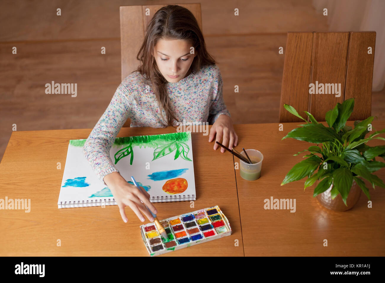Girl sitting at a table painting Stock Photo - Alamy