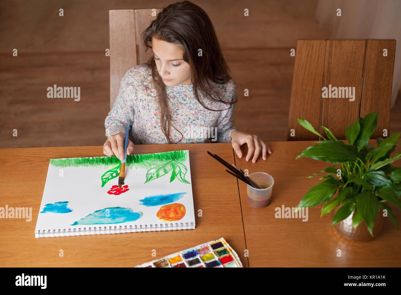 Girl sitting at a table painting Stock Photo - Alamy