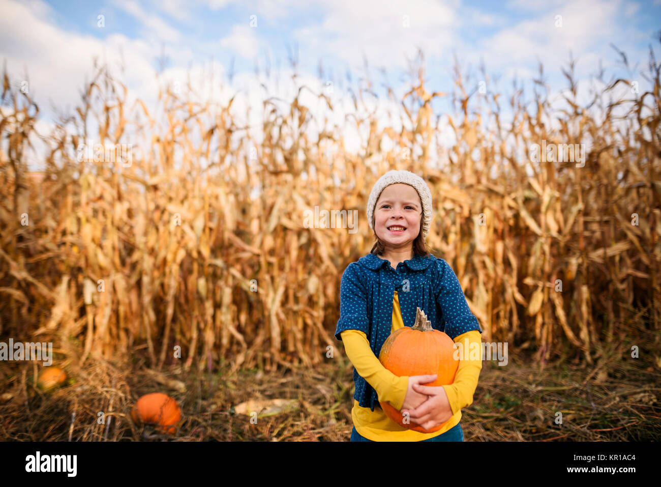 Girl standing in a pumpkin patch holding a pumpkin Stock Photo - Alamy