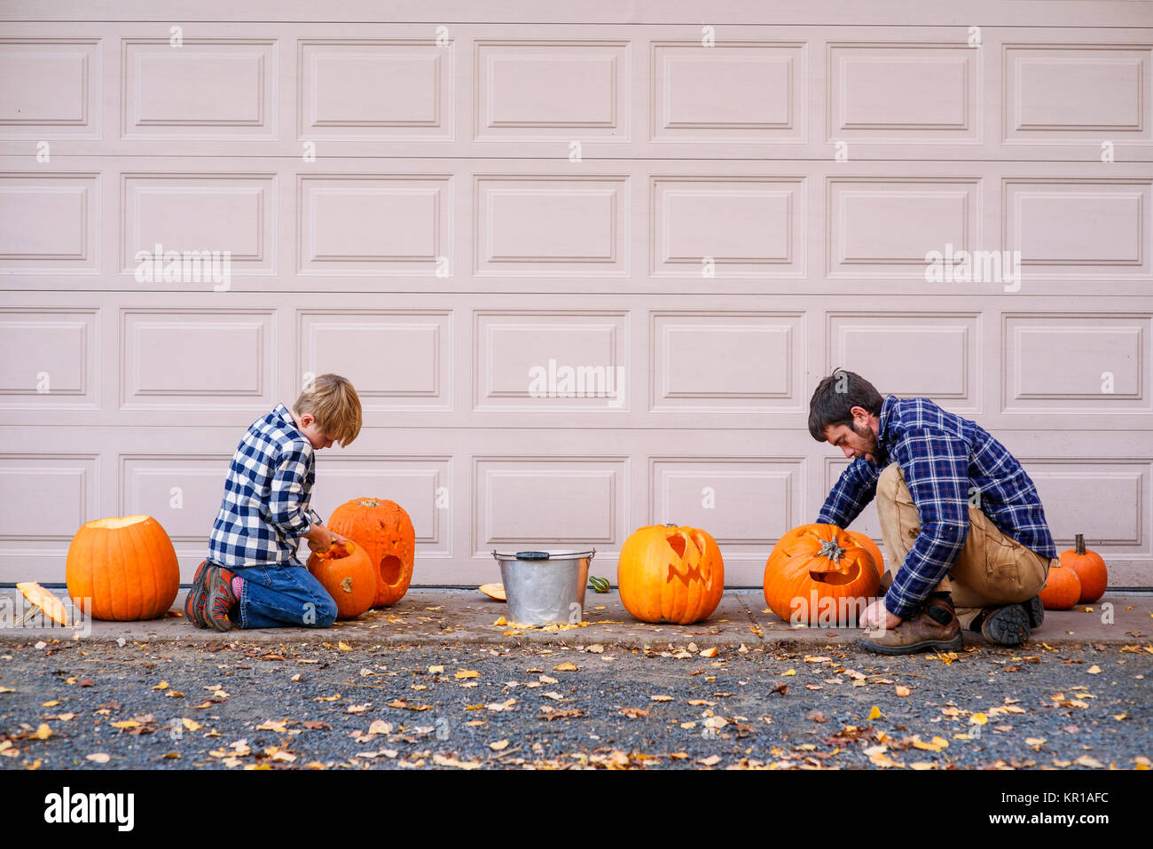 Father And Son Sitting By A Garage Door Carving Halloween Pumpkins
