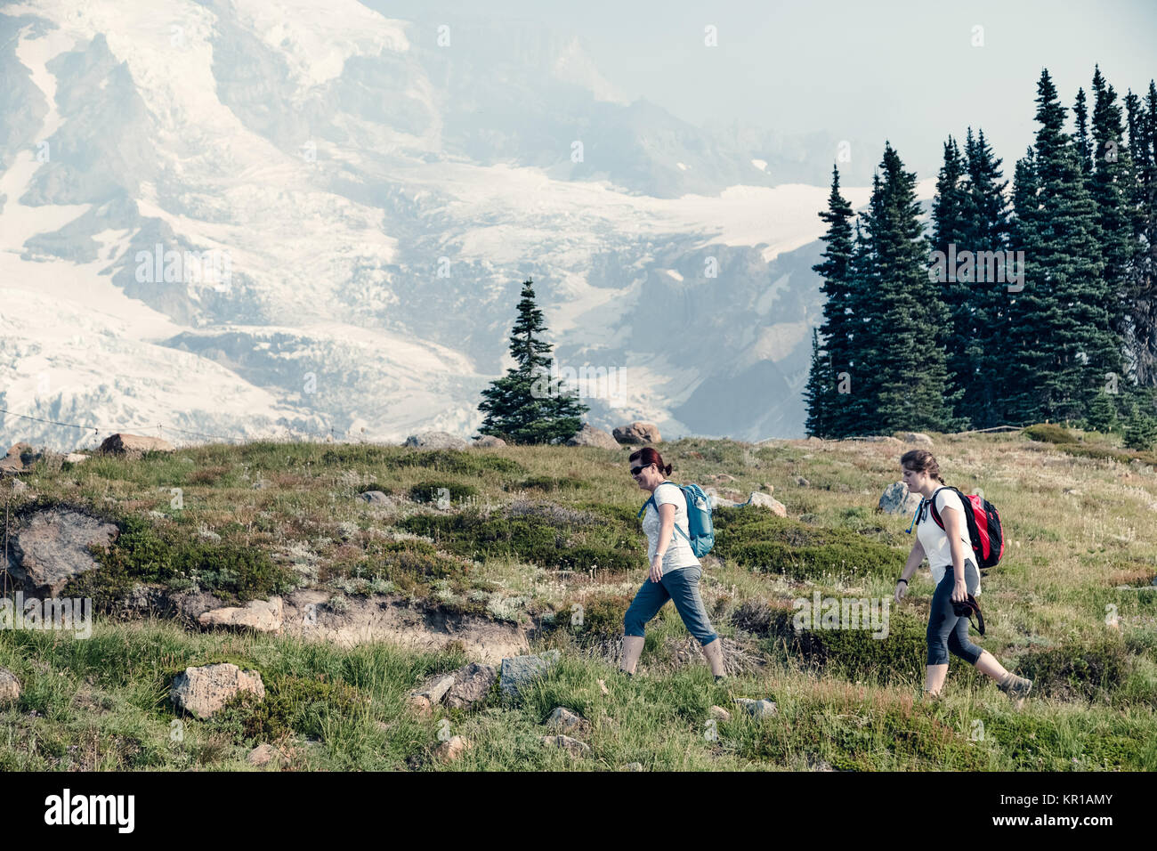 Two women hiking along an alpine trail, Mt Rainier, Washington, United States Stock Photo