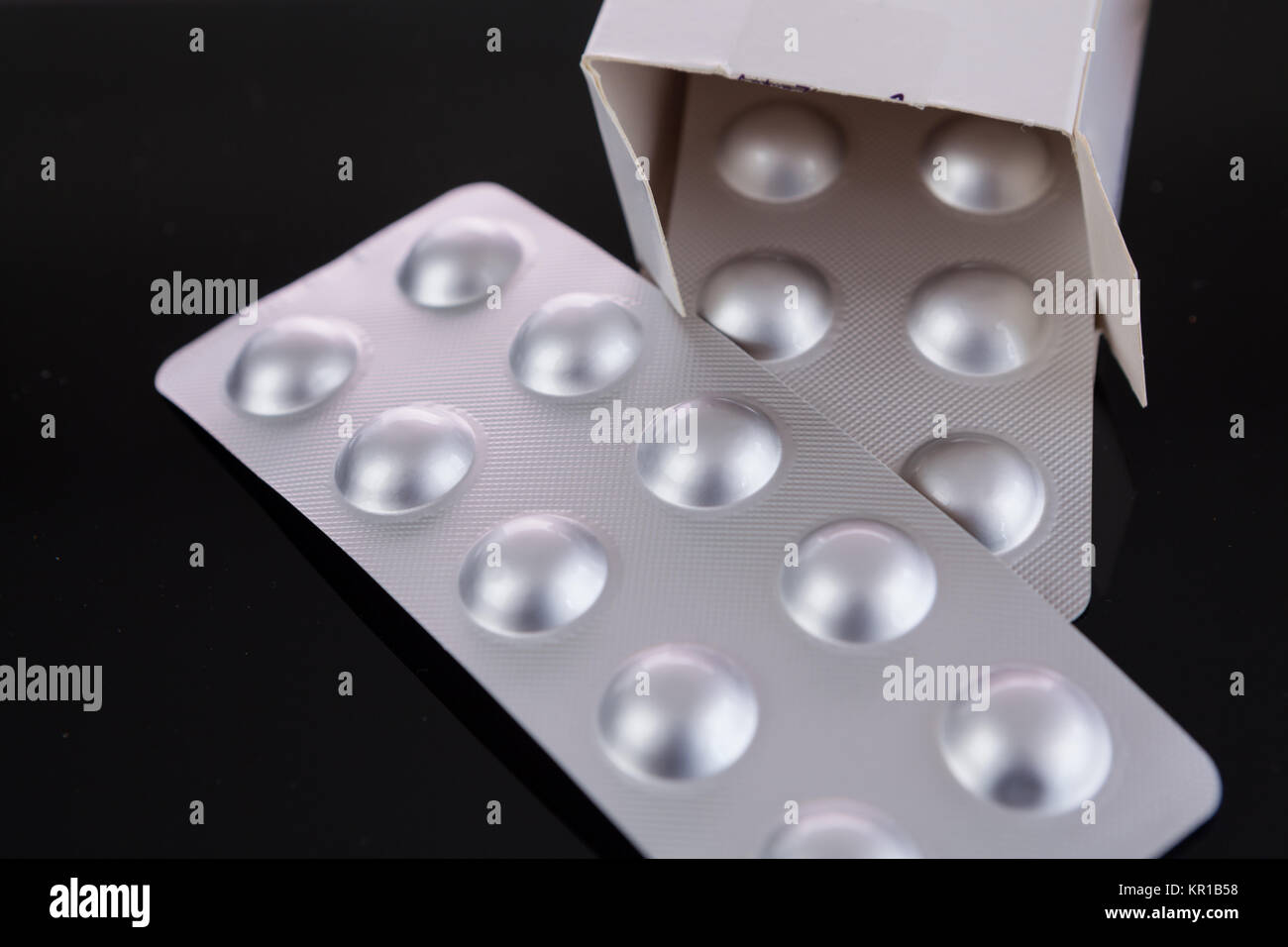 Silberne Blisterpackung von kleinen Pillen zusammen mit Schachtel mit zusätzlichen Packungen durch den offenen Deckel über einem schwarzen Hintergrund in einem Gesundheits-Konzept Stock Photo