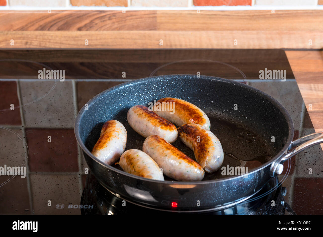 Sausages cooking in a frying pan on an induction hob. Stock Photo