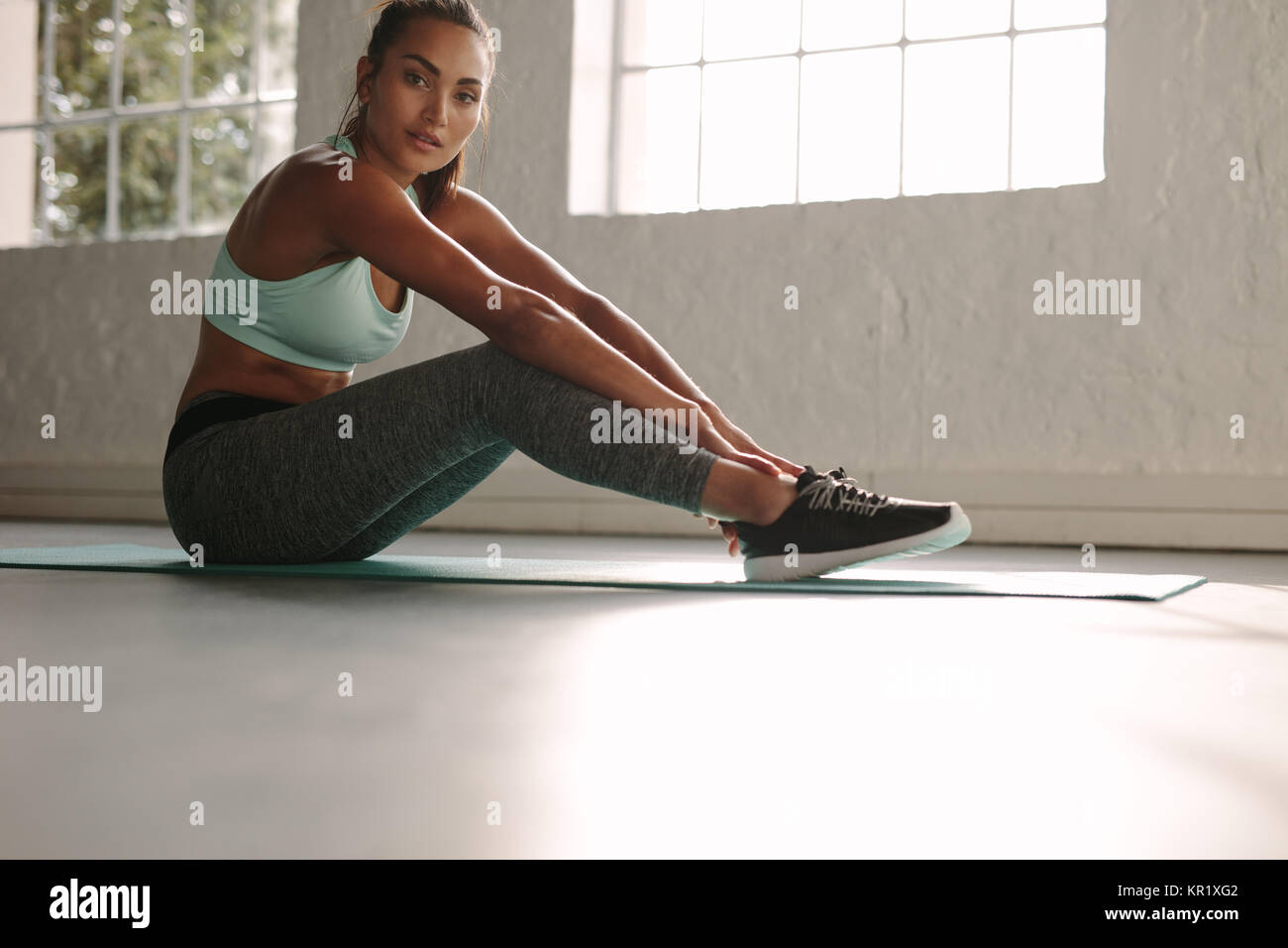 Fit young female sitting on exercise mat in gym. Healthy woman taking ...