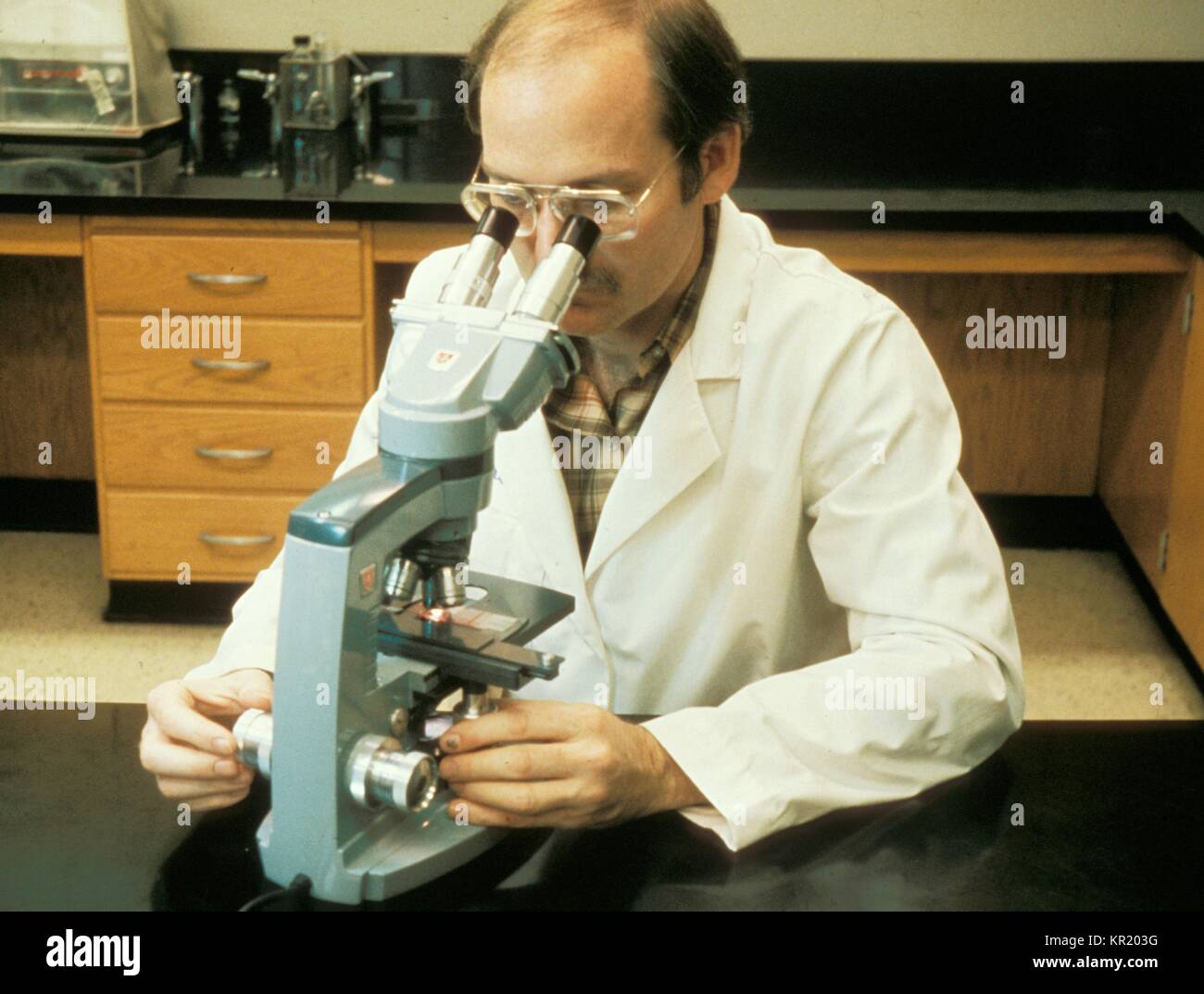 This was Joseph E. McDade, Ph.D. CDC epidemiologist using a transmission light microscope during a scientific investigation, 1977. Dr. McDade isolated and identified the bacterium that caused the outbreak of Legionnaires' disease, an acute and sometimes fatal respiratory illness caused by the Legionella pneumophila bacterium. Image courtesy CDC. Stock Photo