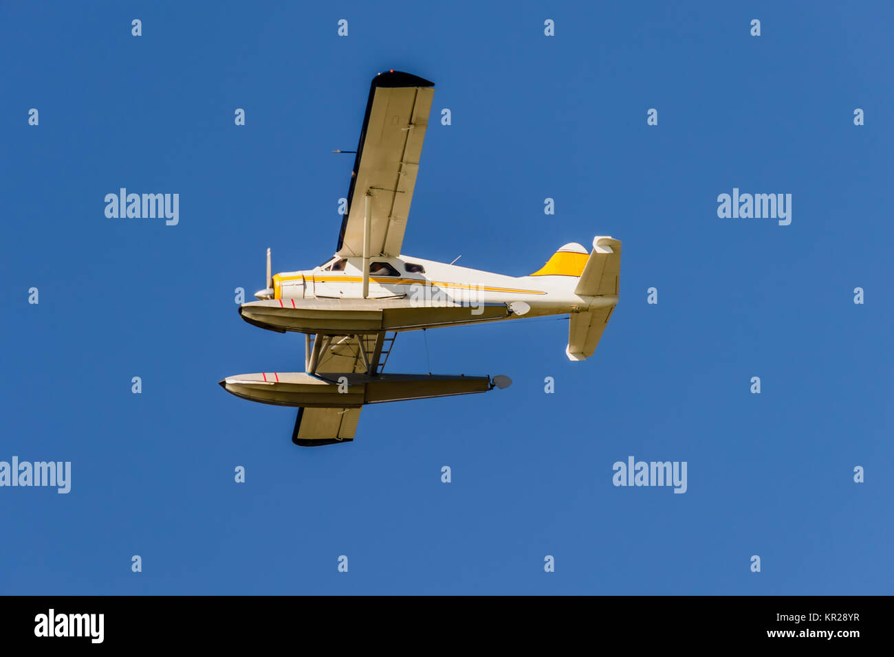view from below on a seaplane with wings, a propeller and a yellow stripe flying in a blue sky Stock Photo